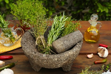 Mortar, different herbs, vegetables and oil on wooden table outdoors