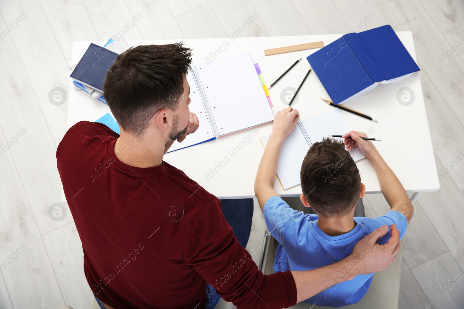 Photo of Dad helping his son with homework in room, above view