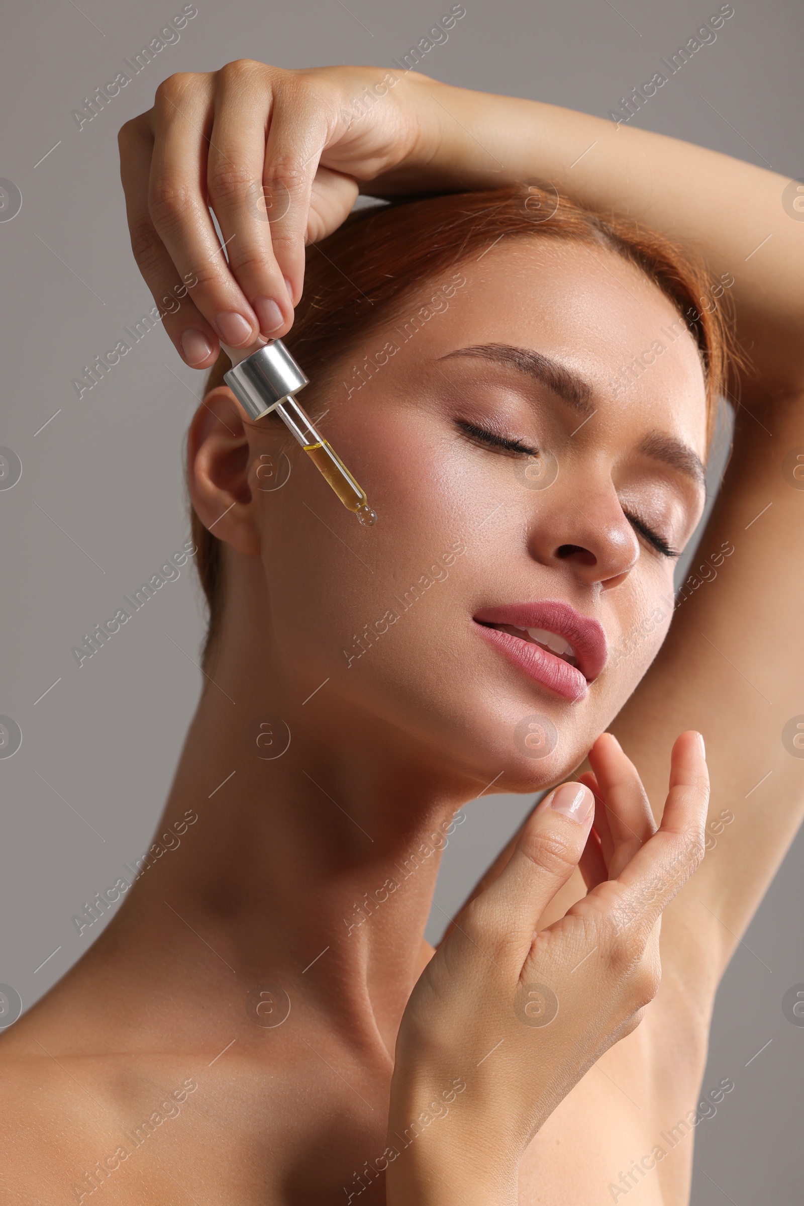 Photo of Beautiful young woman applying cosmetic serum onto her face on grey background