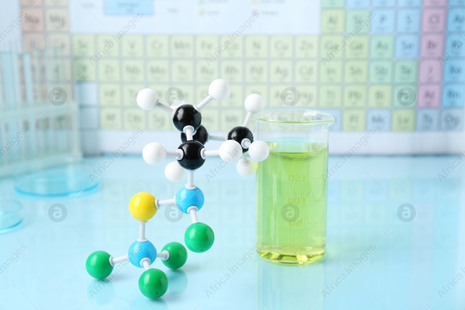 Photo of Molecular model and measuring cup on light surface against periodic table