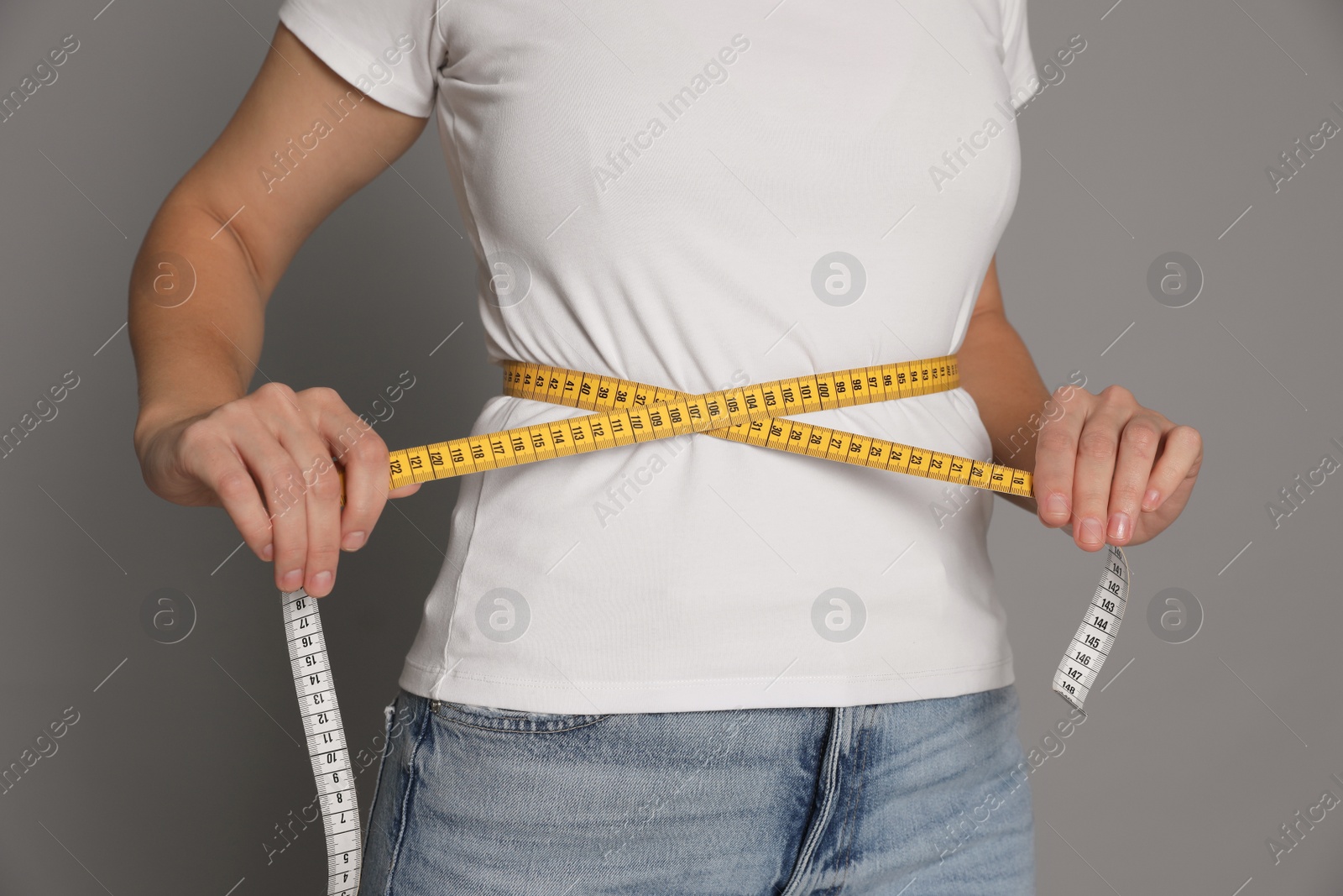 Photo of Woman measuring waist with tape on grey background, closeup