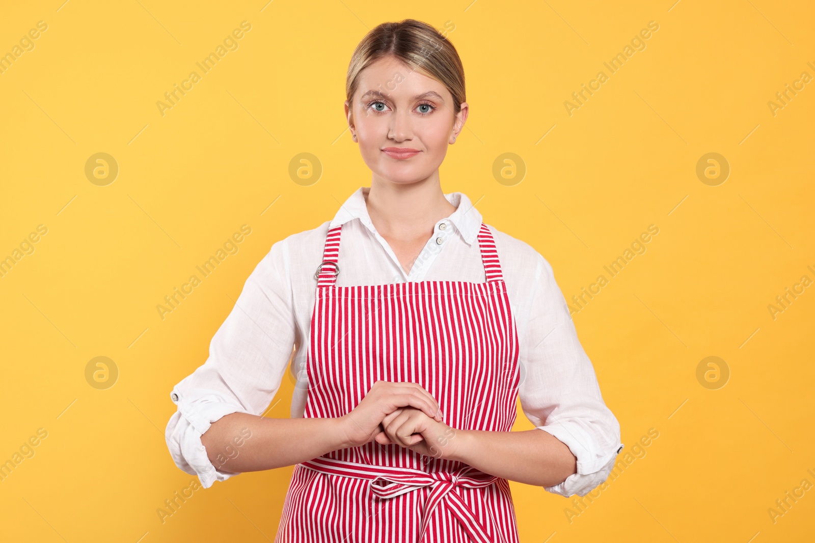 Photo of Beautiful young woman in clean striped apron on orange background