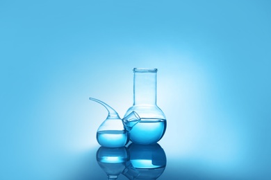 Photo of Laboratory glassware with liquid on table against color background. Chemical analysis