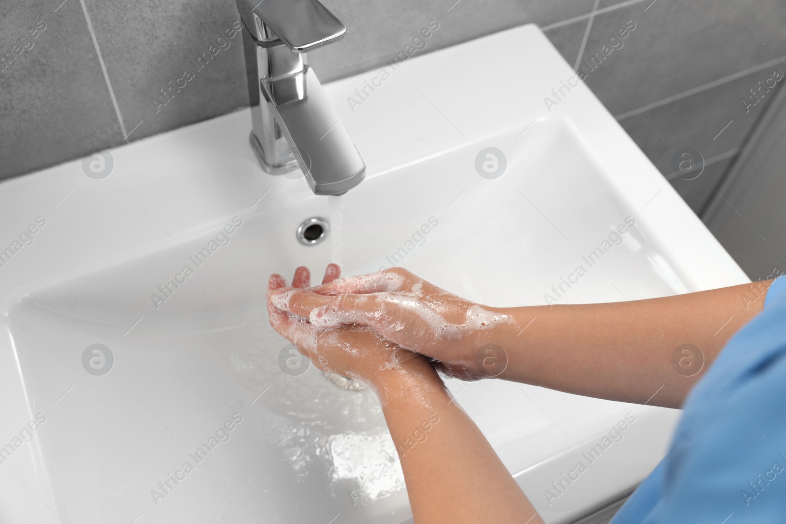 Photo of Doctor washing hands with water from tap in bathroom, above view