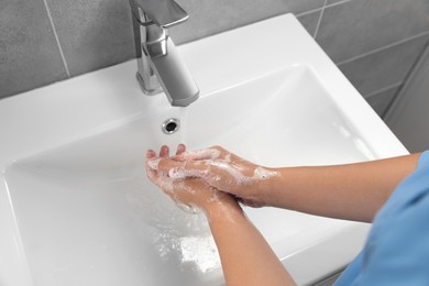 Photo of Doctor washing hands with water from tap in bathroom, above view