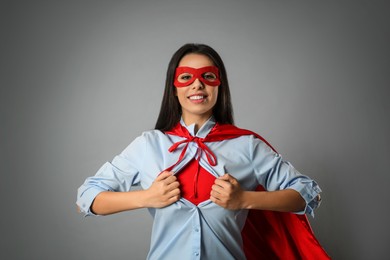 Confident young woman wearing superhero costume under shirt on light grey background