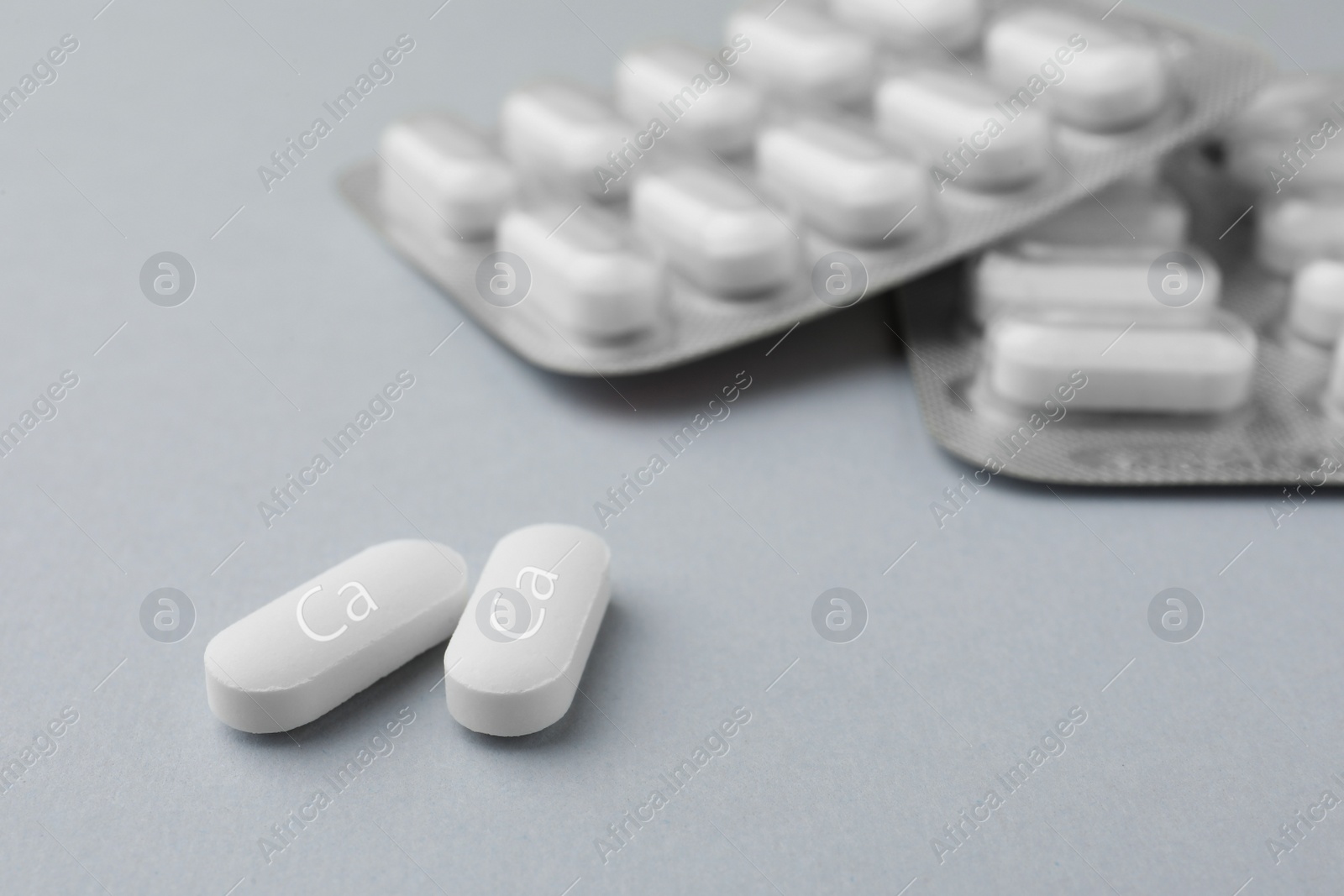 Photo of Calcium supplement pills on light grey background, closeup