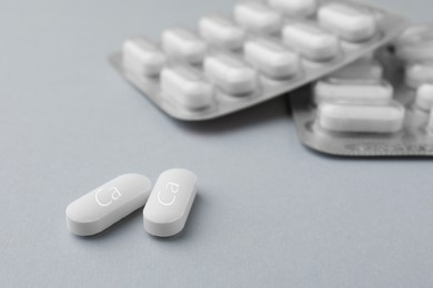Photo of Calcium supplement pills on light grey background, closeup