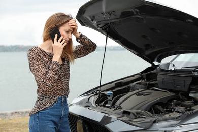 Photo of Troubled young woman talking on phone near broken car outdoors