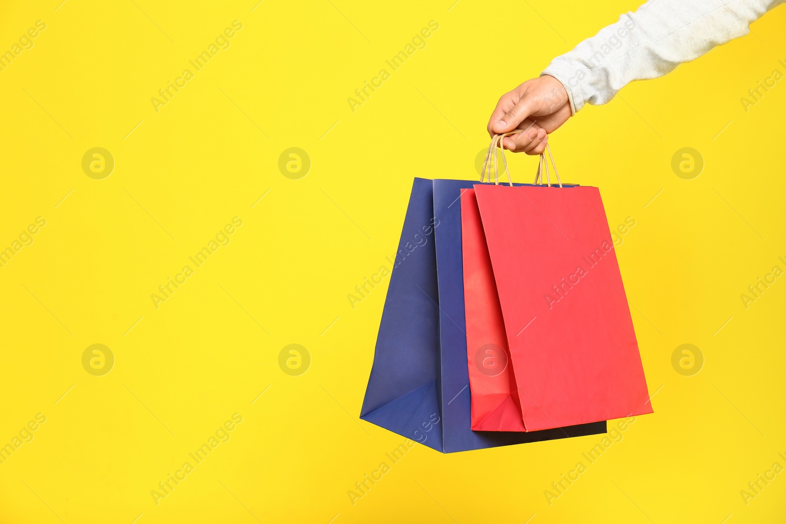 Photo of Young man with paper bags on color background, closeup. Space for text