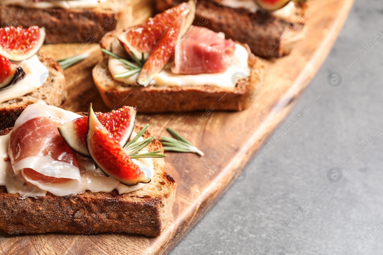 Photo of Bruschettas with cream cheese, prosciutto and figs on grey table, closeup