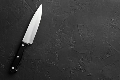 Photo of One sharp knife on dark textured table, top view. Space for text