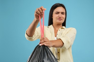 Photo of Woman holding full garbage bag against light blue background, focus on hand