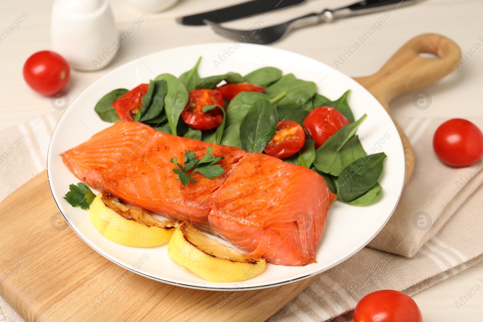 Photo of Tasty grilled salmon with basil, tomatoes and lemon on table