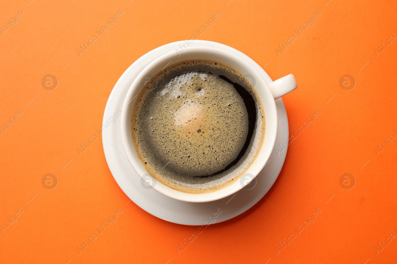 Photo of Fresh coffee in cup on orange background, top view