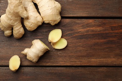 Photo of Cut and whole fresh ginger on wooden table, top view. Space for text