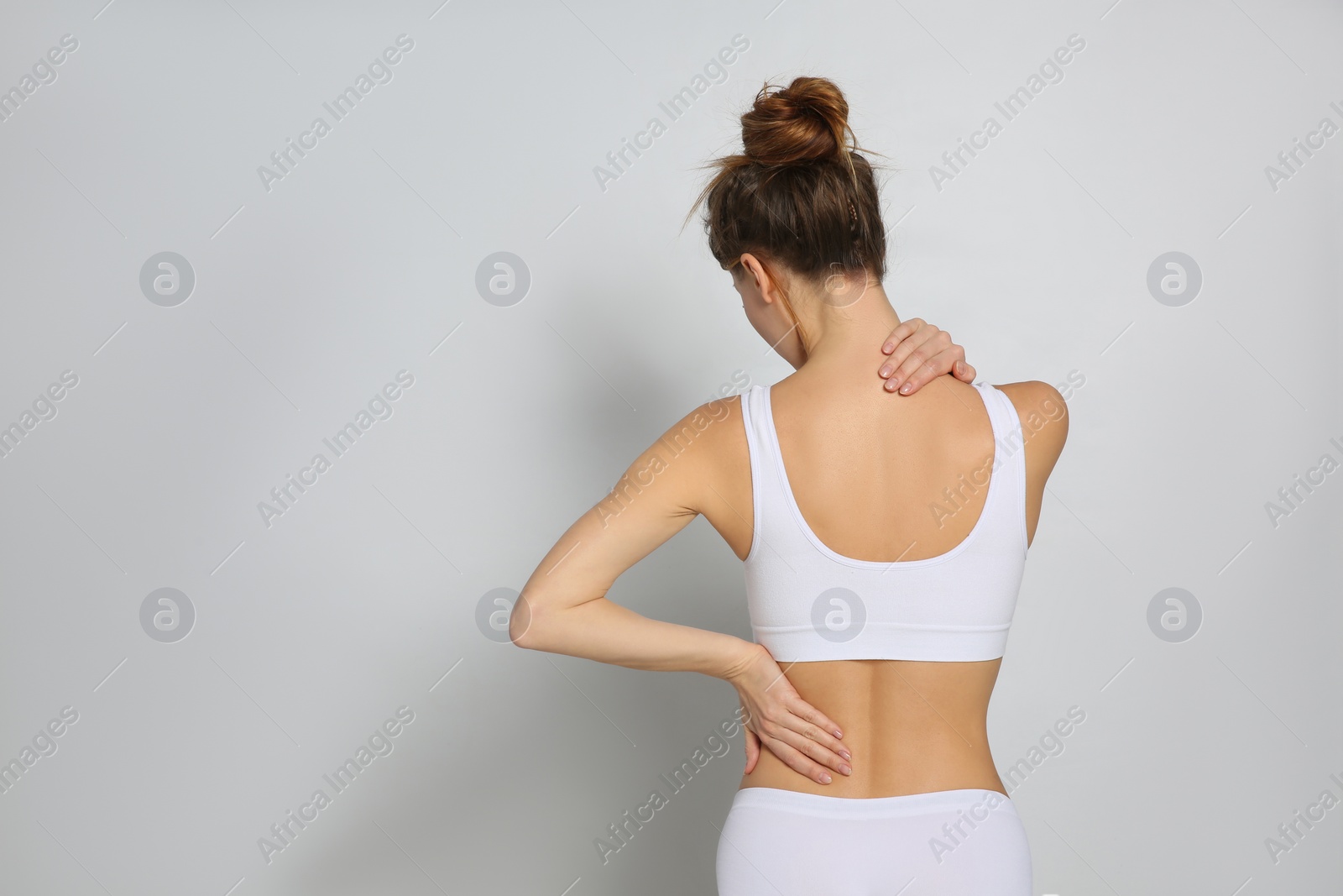 Photo of Woman suffering from pain in back on light grey background. Space for text