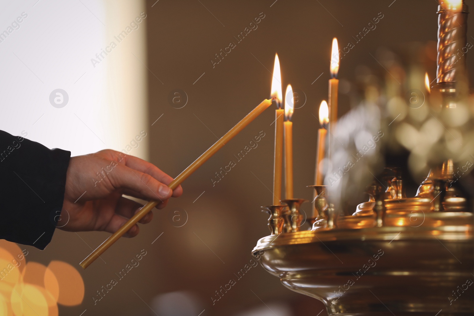 Photo of Man lighting candle near stand in church, closeup. Baptism ceremony