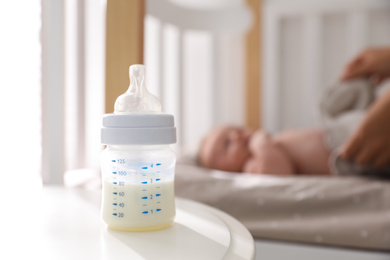 Photo of Mother and little baby indoors, focus on table with bottle of milk