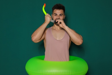 Photo of Funny young man with bright inflatable ring on dark green background