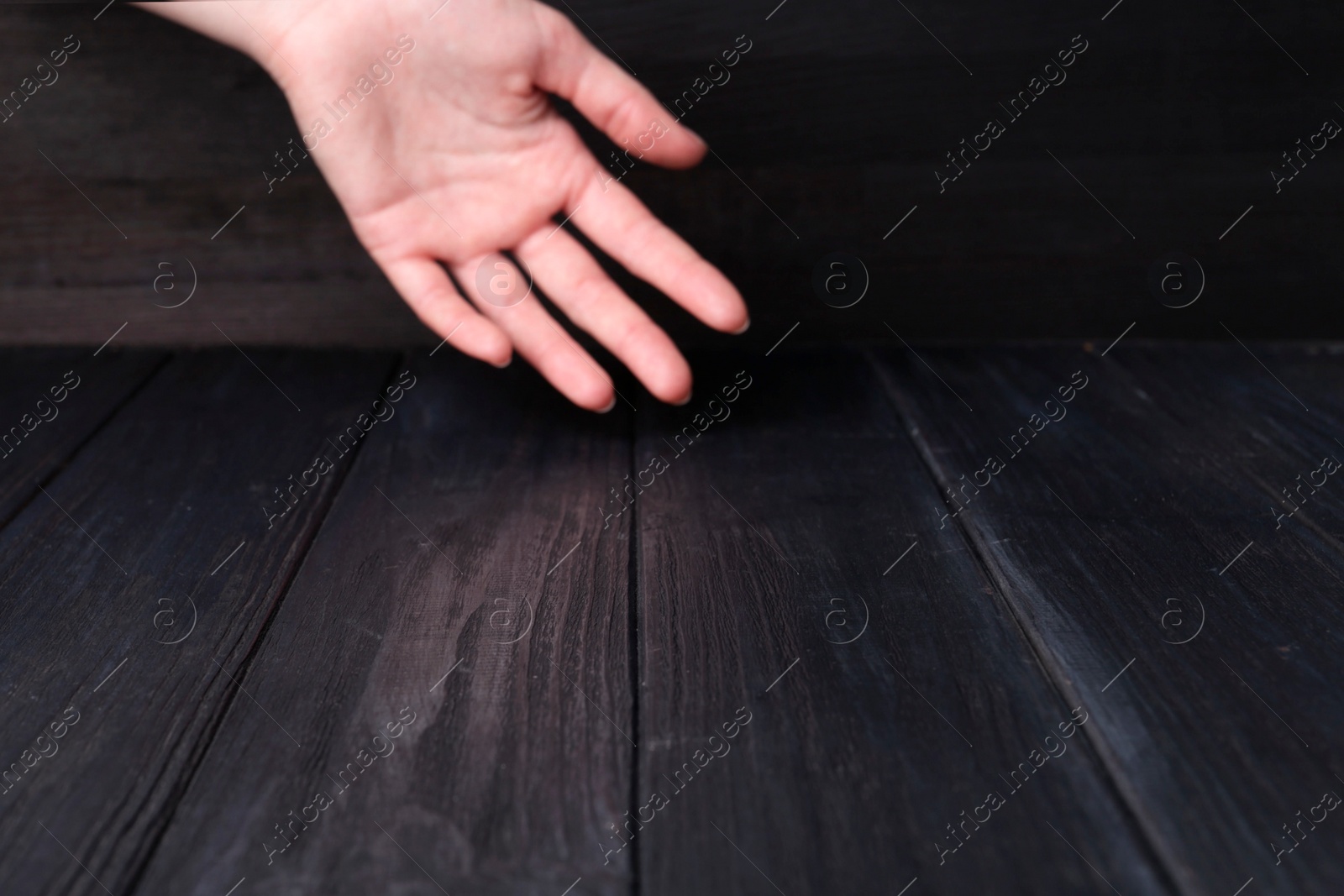 Photo of Woman holding hand above black wooden table, selective focus. Space for text