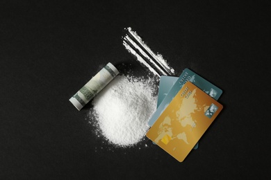 Photo of Composition with cocaine, credit cards and rolled dollar banknote on black background, top view