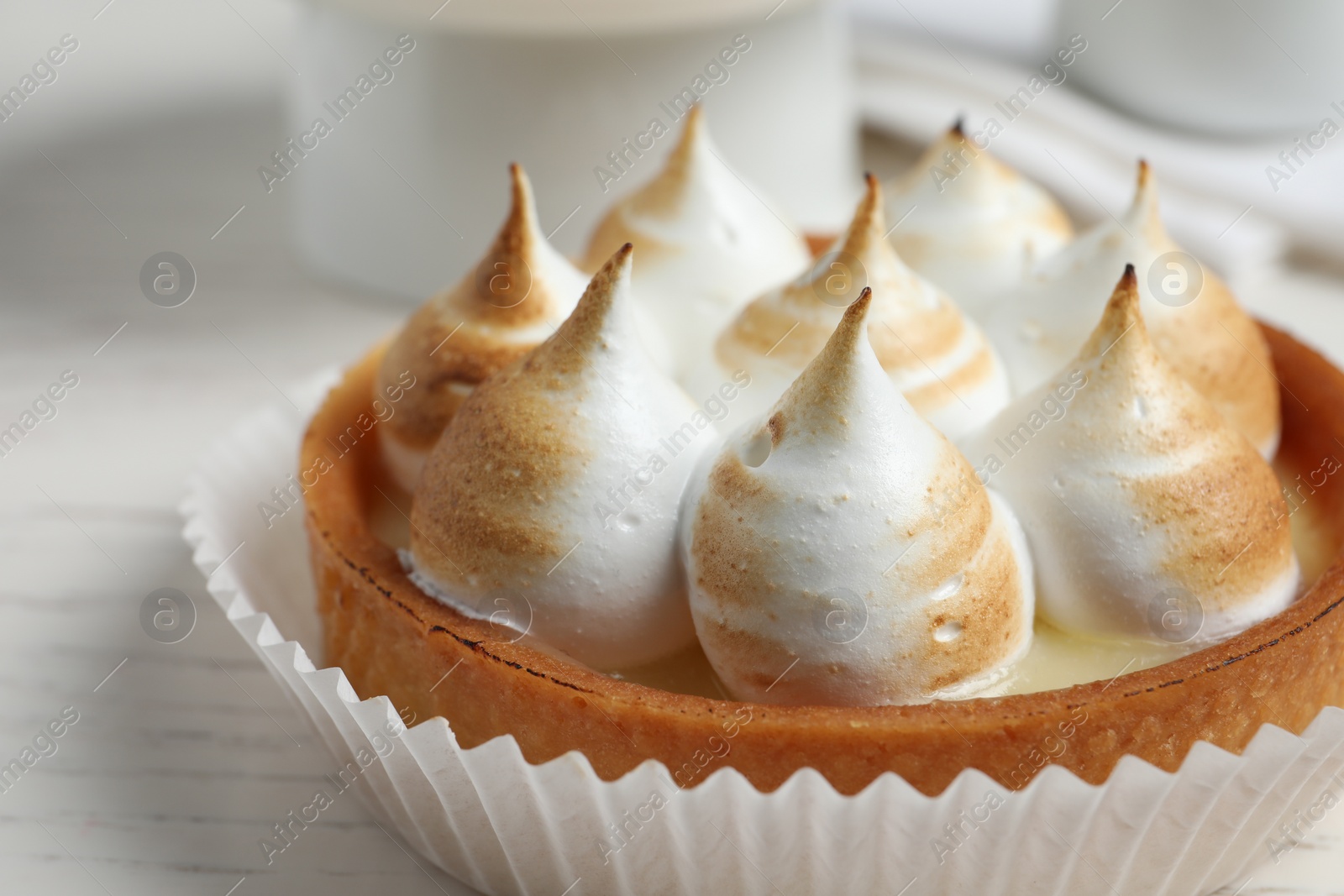 Photo of Tartlet with meringue on white table, closeup. Delicious dessert