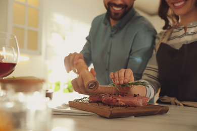 Photo of Lovely young couple cooking meat together in kitchen, closeup