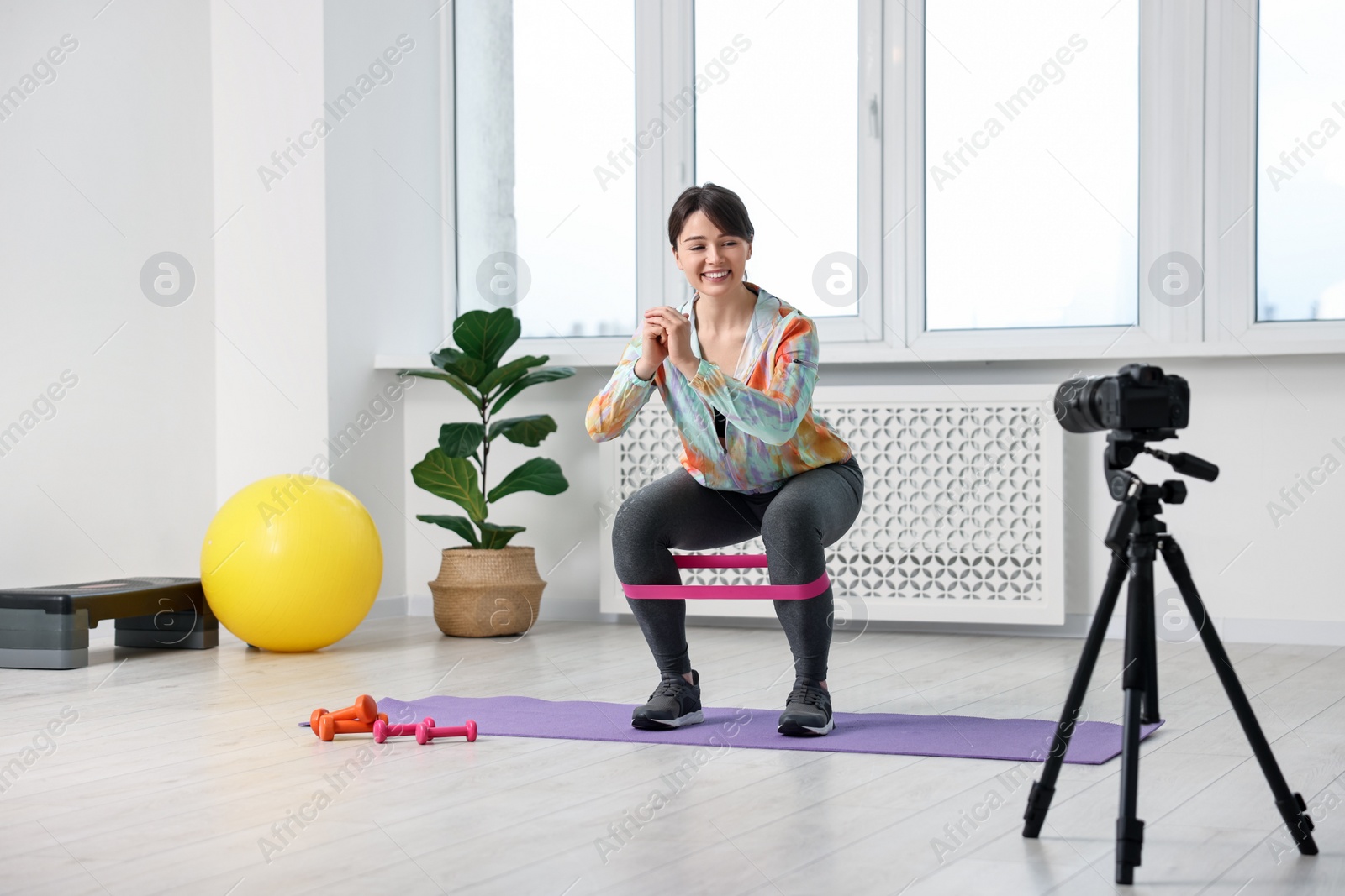 Photo of Happy sports blogger training with resistance band while recording fitness lesson at home