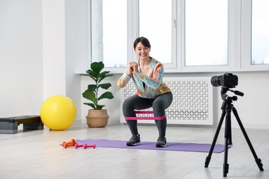 Happy sports blogger training with resistance band while recording fitness lesson at home