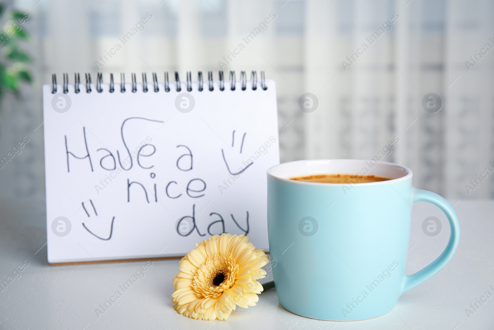 Photo of Delicious morning coffee, beautiful flower and HAVE A NICE DAY wish on white table indoors
