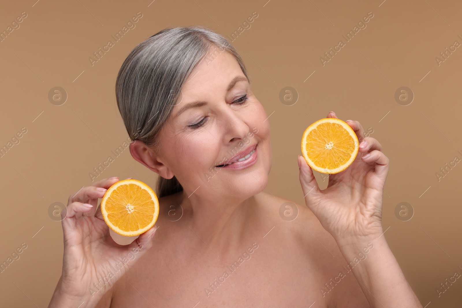 Photo of Beautiful woman with halves of orange rich in vitamin C on beige background