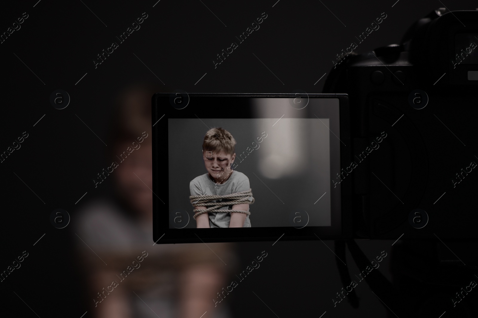 Photo of Little boy with bruises tied up and taken hostage on dark background, view through camera screen