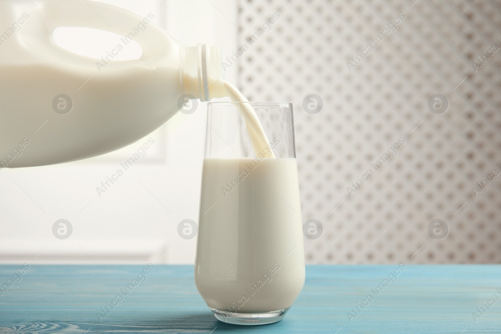 Photo of Pouring milk from gallon bottle into glass on blue wooden table