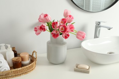 Vase with beautiful pink tulips and toiletries near sink in bathroom