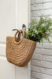 Photo of Stylish beach bag with beautiful wildflowers hanging on door handle