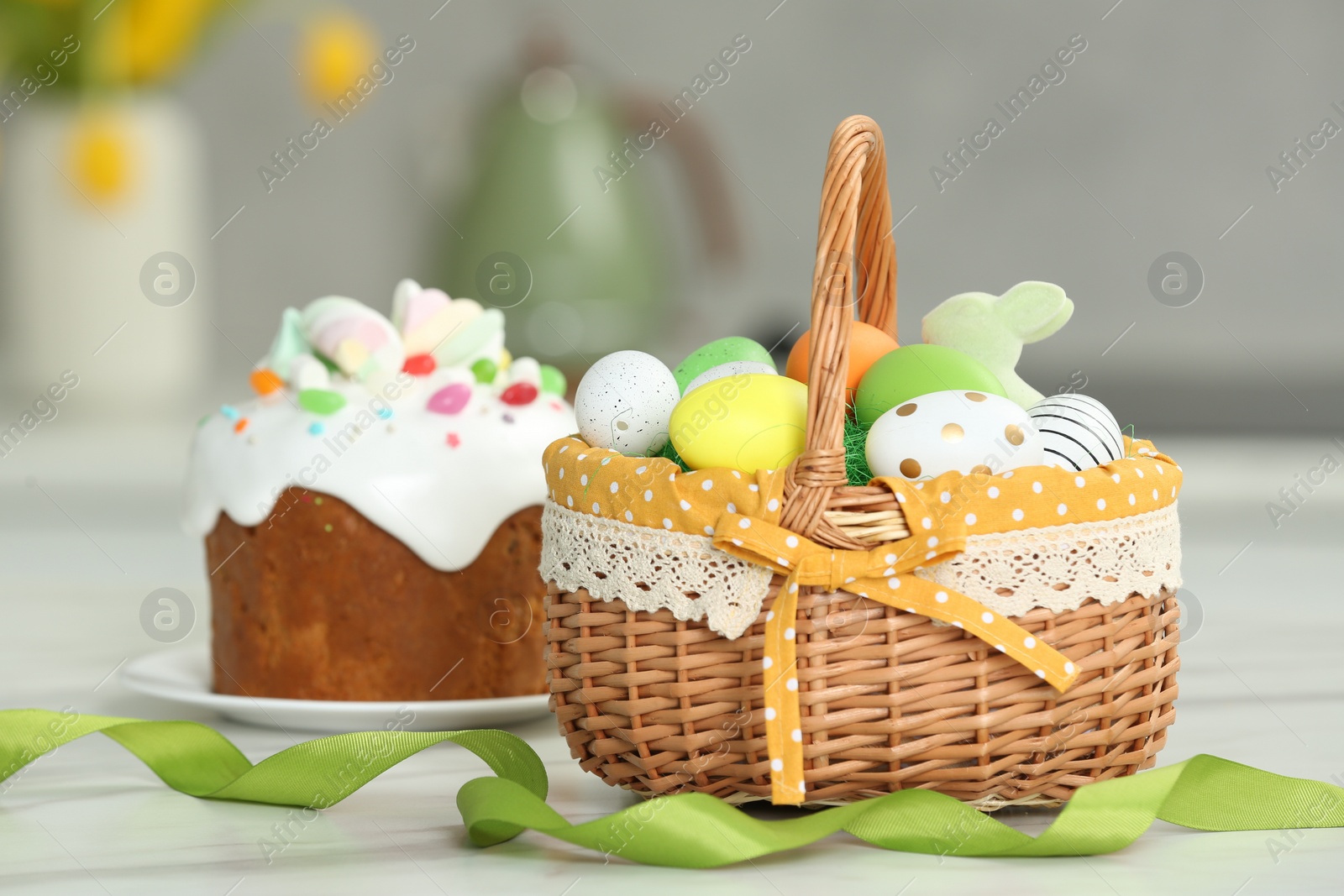 Photo of Easter basket with painted eggs near tasty cake on white marble table