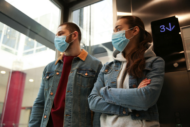 Photo of Couple wearing disposable masks in elevator. Dangerous virus