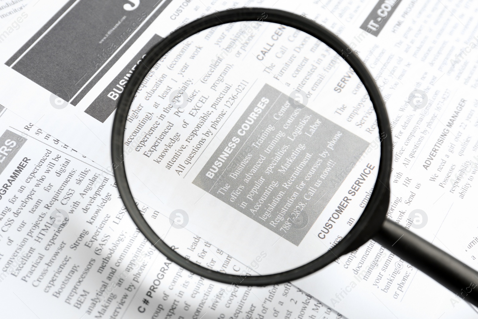 Photo of Looking through magnifying glass at newspaper, closeup. Job search concept