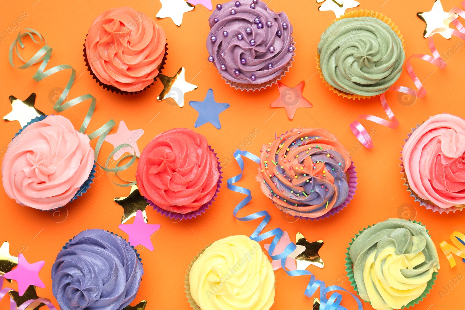 Photo of Delicious cupcakes with bright cream and party decor on orange background, flat lay