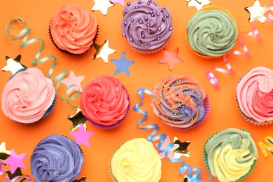 Photo of Delicious cupcakes with bright cream and party decor on orange background, flat lay