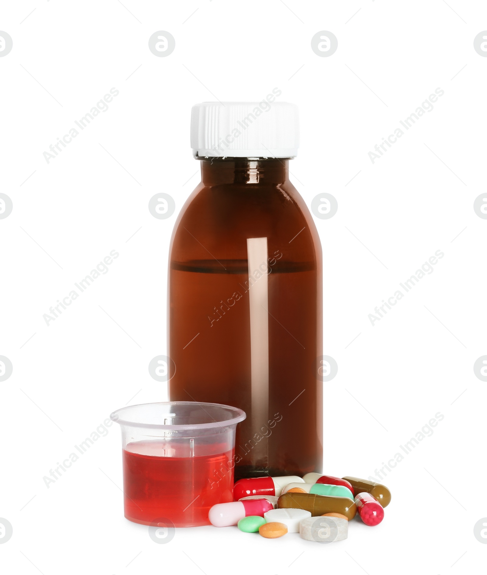 Photo of Bottle of cough syrup, measuring cup and pills on white background