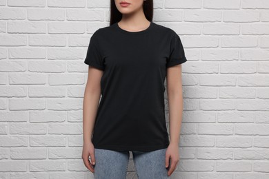 Woman wearing stylish black T-shirt near white brick wall, closeup