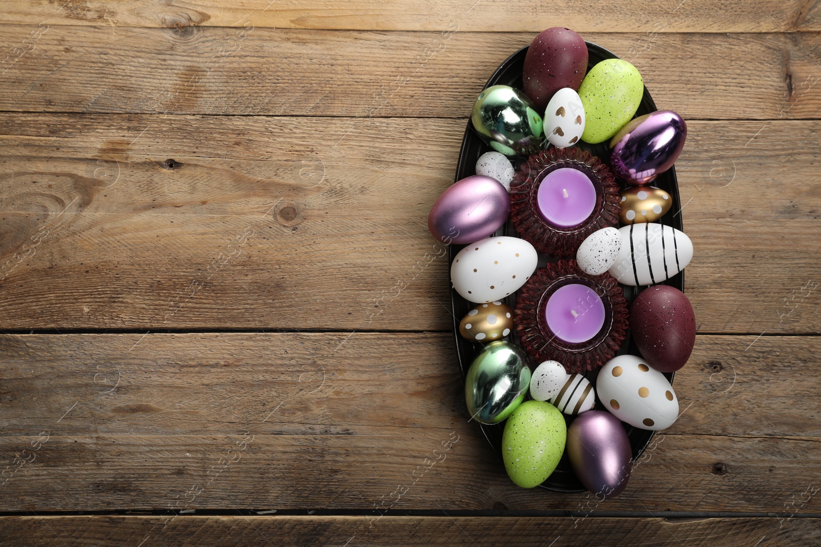 Photo of Many beautifully decorated Easter eggs and scented candles on wooden table, top view. Space for text