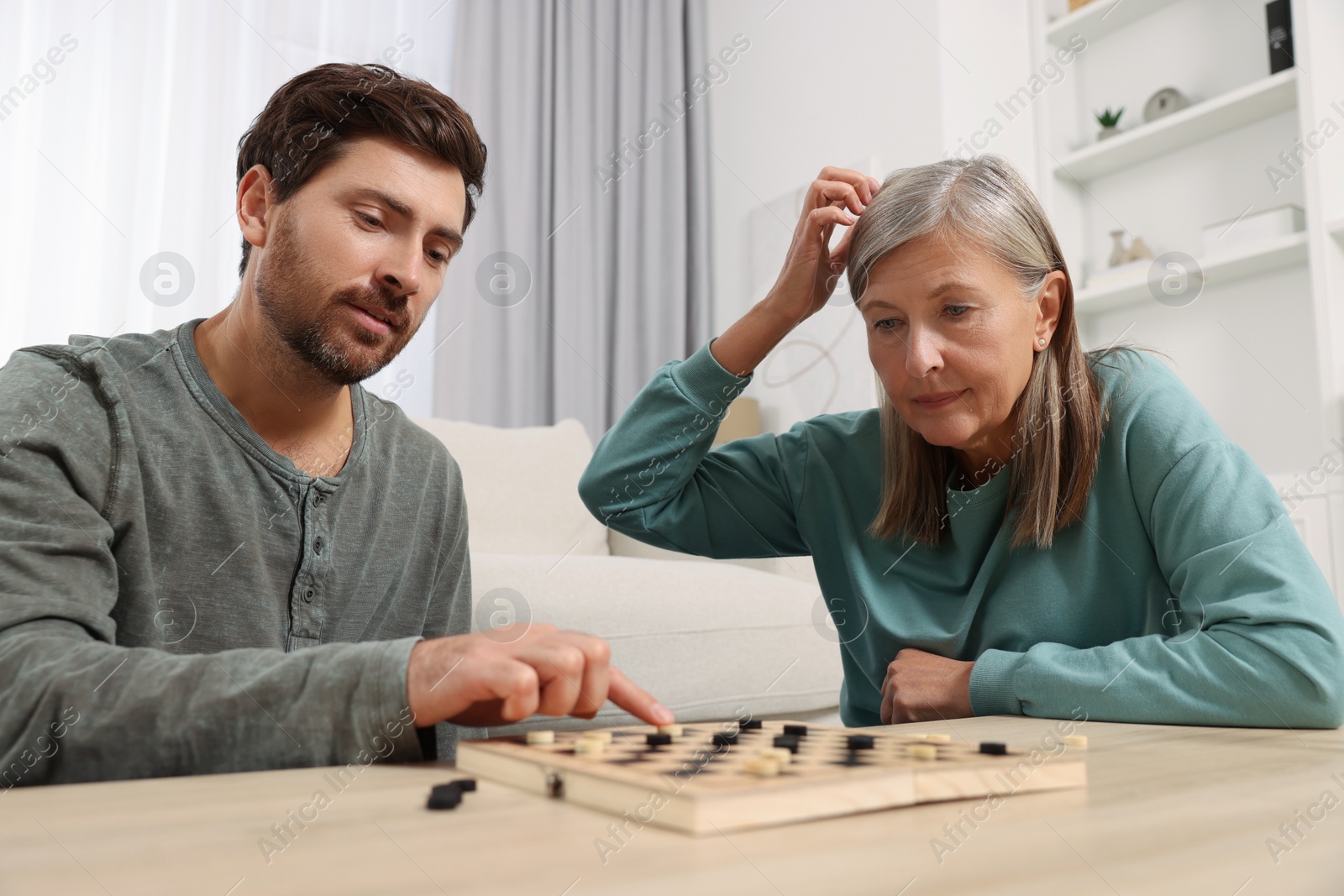 Photo of Family playing checkers at wooden table in room