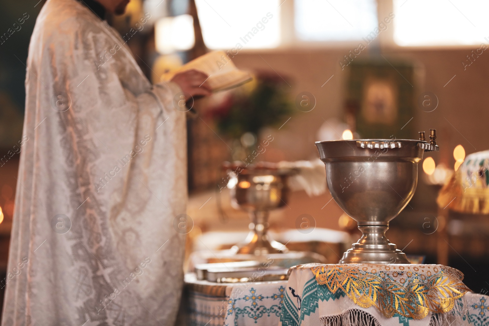 Photo of MYKOLAIV, UKRAINE - FEBRUARY 27, 2021: Priest conducting baptism ceremony in Kasperovskaya icon of Mother of God cathedral, focus on vessel with holy water