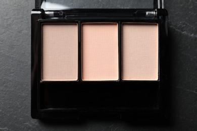 Nude eye shadow palette on dark grey textured table, top view