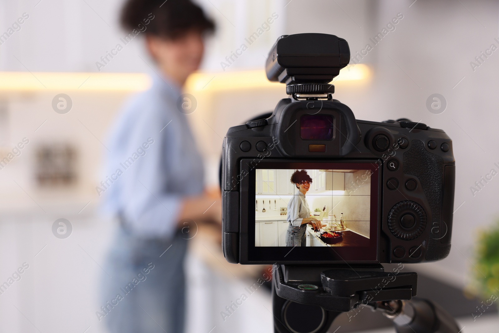 Photo of Food blogger cooking while recording video in kitchen, focus on camera