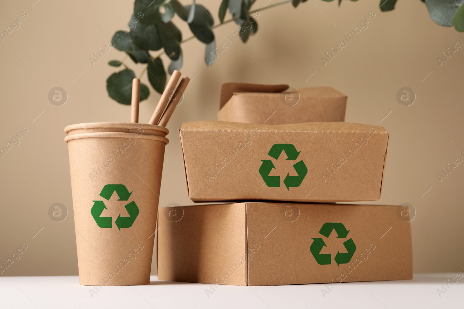 Image of Set of eco friendly food packaging with recycling symbols on white table against beige background