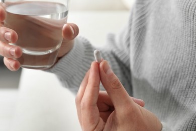 Photo of Man with glass of water and pill on blurred background, closeup